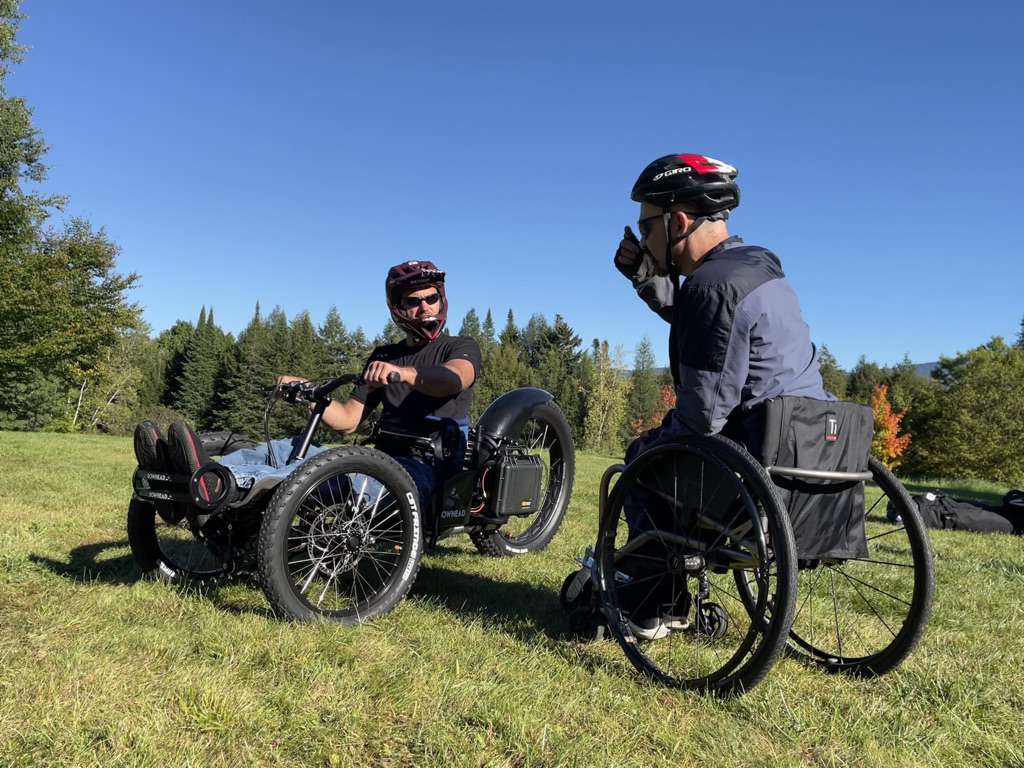 Man in wheelchair talks to man in adaptive mountain bike.